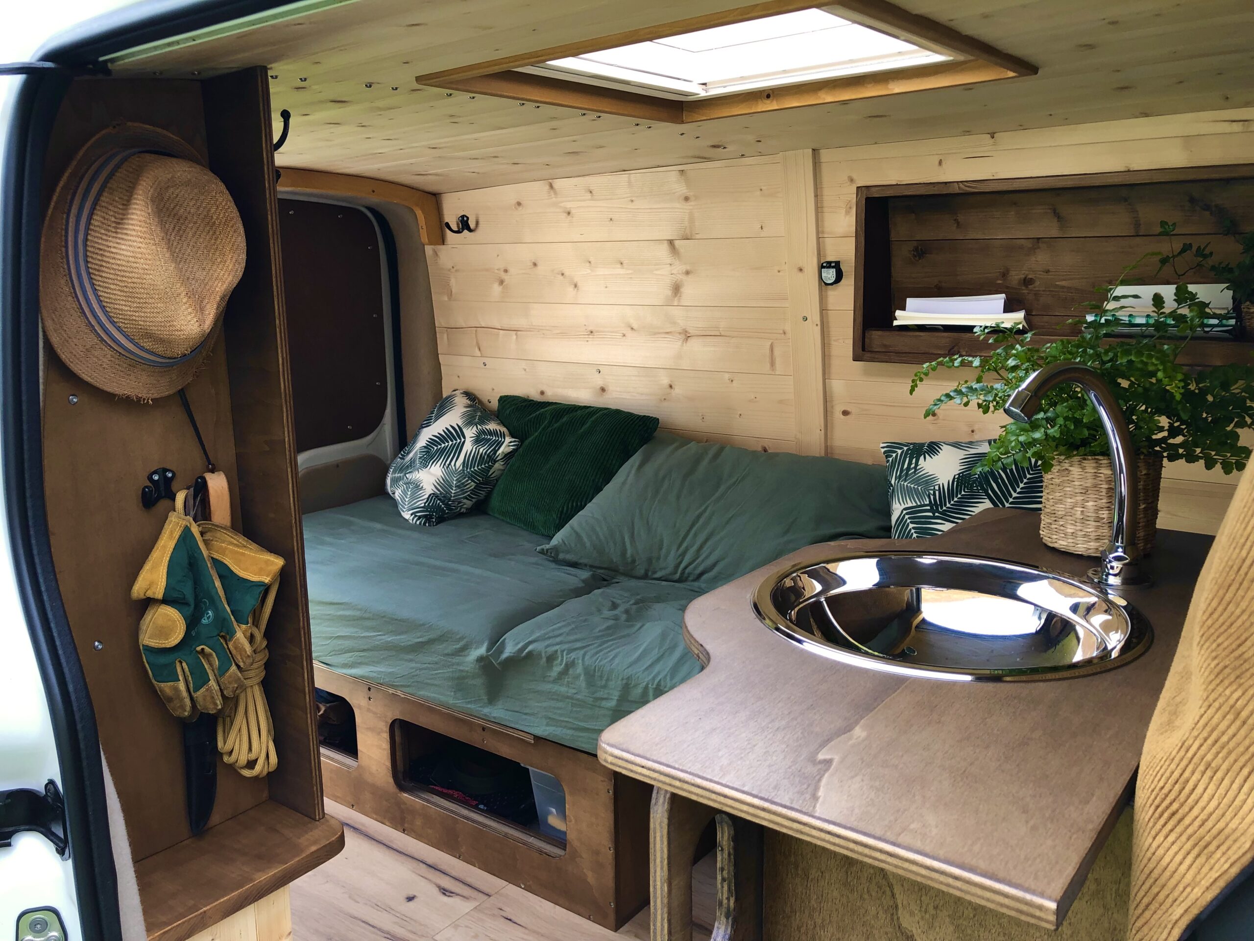 Aménagement intérieur d’un van aménagé avec du bois, disposant d'un lit peigne, d'un coin cuisine, rangements et espace cosy pour la vie en van